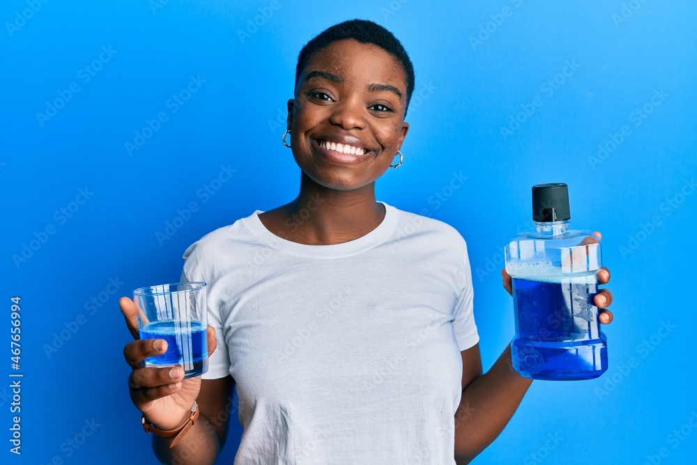 Young african american woman holding mouthwash for fresh breath smiling with a happy and cool smile on face. showing teeth. Young african american woman holding mouthwash for fresh breath smiling with a happy and cool smile on face. showing teeth.
