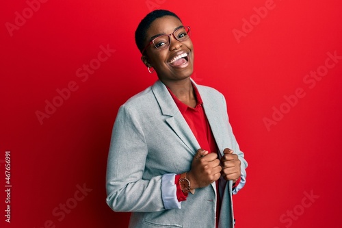 Young african american woman wearing business jacket and glasses winking looking at the camera with sexy expression, cheerful and happy face. photo