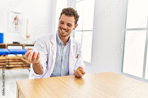 Young hispanic man wearing physiotherapist uniform press anti stress ball at clinic