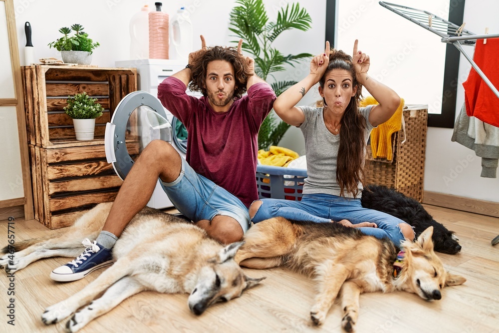 Obraz premium Young hispanic couple doing laundry with dogs doing funny gesture with finger over head as bull horns