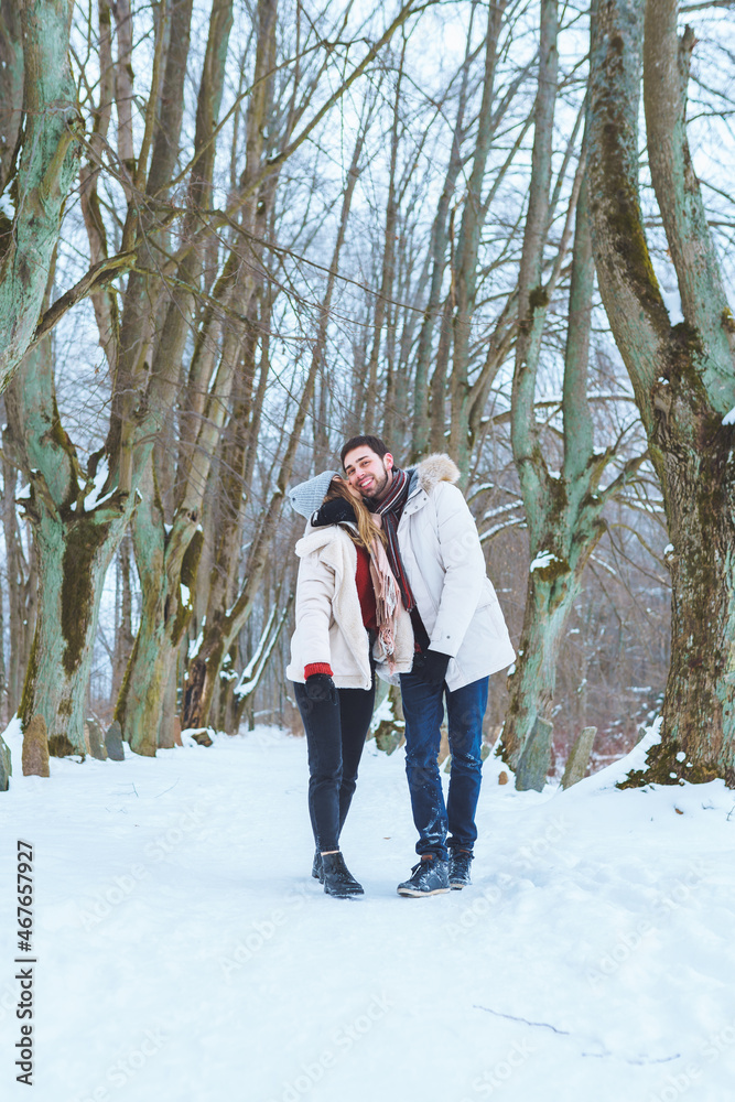 Young happy couple kiss each other and walk in winter park holding hands. Man and woman have fun together during winter holidays.