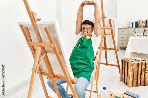 Young hispanic man smiling confident stretching arms at art studio