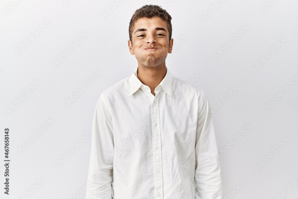 Young handsome hispanic man standing over isolated background puffing cheeks with funny face. mouth inflated with air, crazy expression. Young handsome hispanic man standing over isolated background puffing cheeks with funny face. mouth inflated with air, crazy expression.