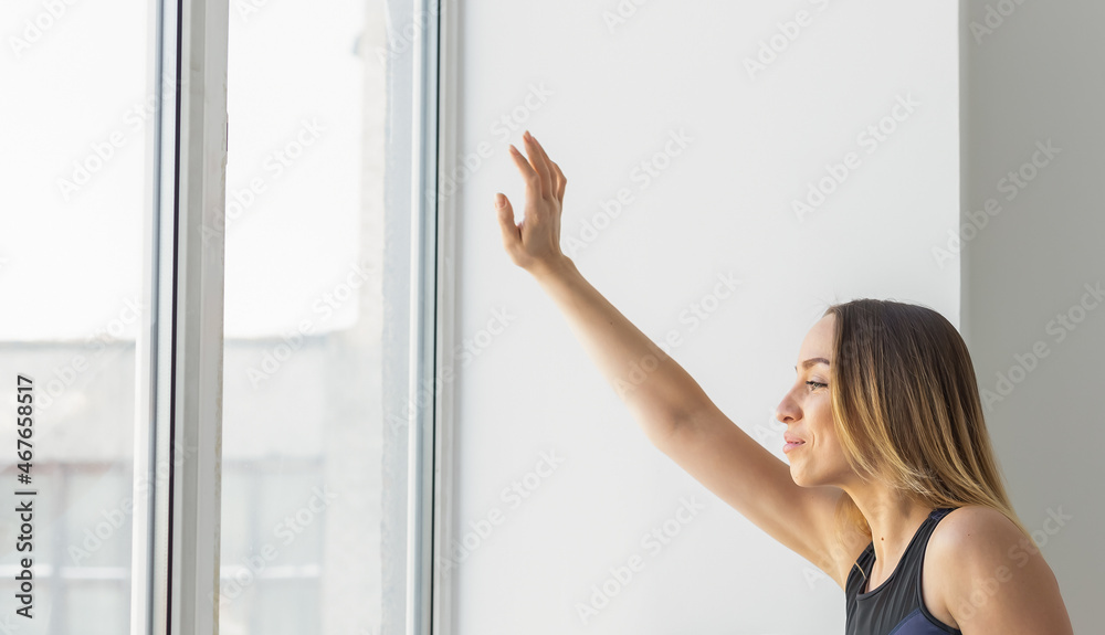 Beautiful young woman looking out at the window for hello and waving to someone. Copy space and space for advertising Beautiful young woman looking out at the window for hello and waving to someone. Copy space and space for advertising