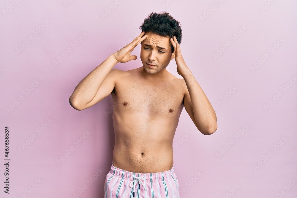 Fototapeta premium Young handsome man wearing swimwear shirtless with hand on head for pain in head because stress. suffering migraine.