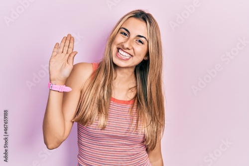 Beautiful hispanic woman wearing casual summer t shirt waiving saying hello happy and smiling, friendly welcome gesture