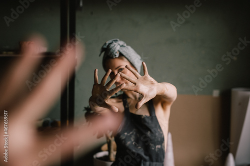 beautiful sculptor girl with a headband and a black apron shows her hands stained with clay. focus of camera is on girl's fingers. concept is beauty and art.