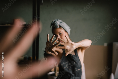 beautiful sculptor girl with a headband and a black apron shows her hands stained with clay. focus of camera is on girl's fingers. concept is beauty and art.