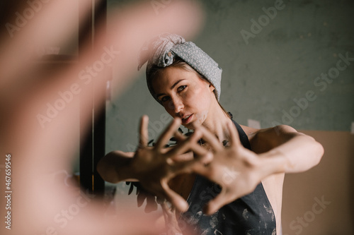 beautiful sculptor girl with a headband and a black apron shows her hands stained with clay. camera focus is on girl's face, blur is on her hands.