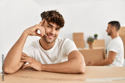 Two hispanic men couple smiling confident leaning on cardboard box at new home