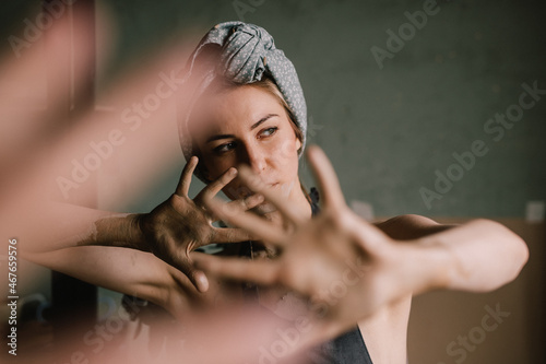beautiful sculptor girl with a headband and a black apron shows her hands stained with clay. camera focus is on girl's face, blur is on her hands.