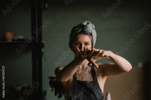 beautiful sculptor girl with a headband and a black apron shows her hands stained with clay. focus of camera is on girl's fingers. concept is beauty and art.