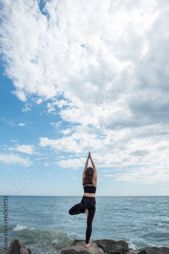 Tree pose. Meditating woman. Peaceful yoga. Unrecognizable lady standing in Vrikshasana on rock stone namaste hands looking sea view. photo