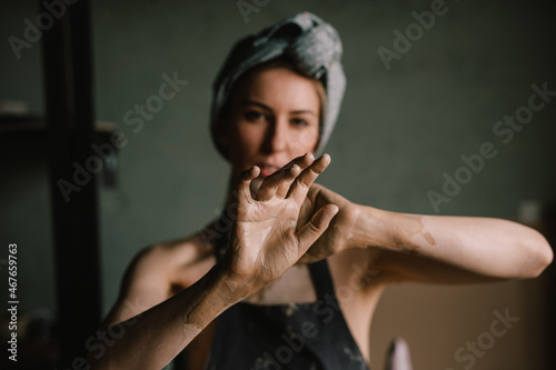 beautiful sculptor girl with a headband and a black apron shows her hands stained with clay. focus of camera is on girl's fingers. concept is beauty and art.