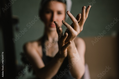 beautiful sculptor girl with a headband and a black apron shows her hands stained with clay. focus of camera is on girl's fingers. concept is beauty and art.