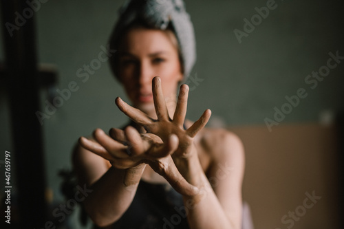 beautiful sculptor girl with a headband and a black apron shows her hands stained with clay. focus of camera is on girl's fingers. concept is beauty and art.