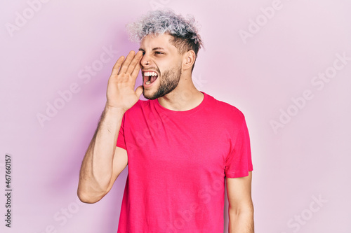 Young hispanic man with modern dyed hair wearing casual pink t shirt shouting and screaming loud to side with hand on mouth. communication concept.