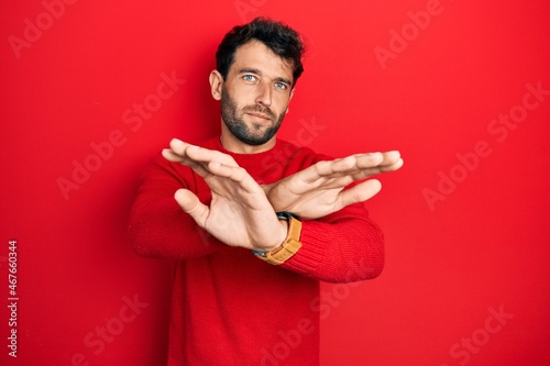 Handsome man with beard wearing casual red sweater rejection expression crossing arms doing negative sign, angry face