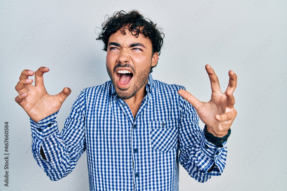 Fototapeta premium Young hispanic man wearing casual clothes crazy and mad shouting and yelling with aggressive expression and arms raised. frustration concept.