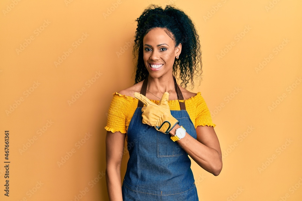 Middle age african american woman wearing professional apron cheerful with a smile on face pointing with hand and finger up to the side with happy and natural expression Middle age african american woman wearing professional apron cheerful with a smile on face pointing with hand and finger up to the side with happy and natural expression