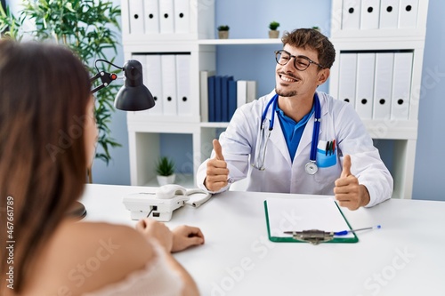 Young doctor with client at medical clinic success sign doing positive gesture with hand, thumbs up smiling and happy. cheerful expression and winner gesture.