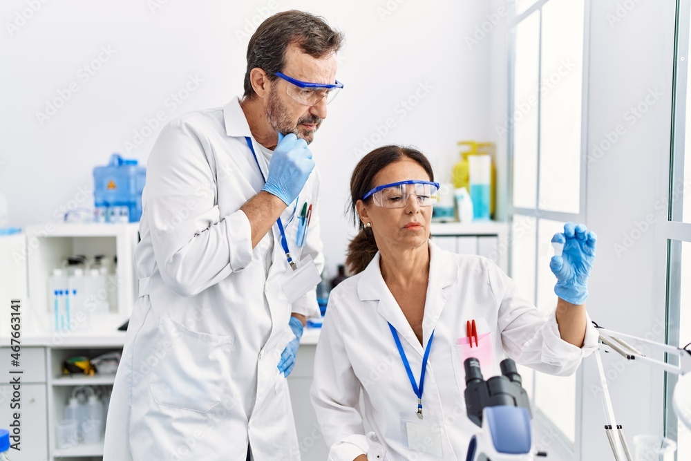 Middle age man and woman partners wearing scientist uniform analyzing sample at laboratory Middle age man and woman partners wearing scientist uniform analyzing sample at laboratory