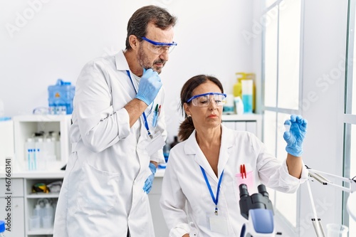Middle age man and woman partners wearing scientist uniform analyzing sample at laboratory