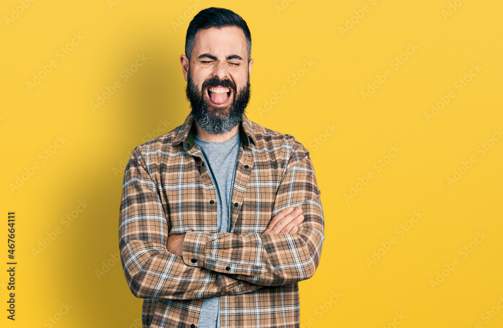 Hispanic man with beard with arms crossed gesture sticking tongue out happy with funny expression. Hispanic man with beard with arms crossed gesture sticking tongue out happy with funny expression.