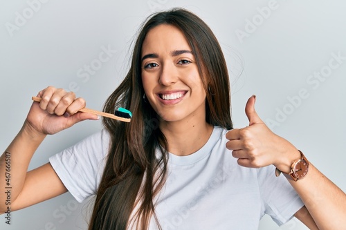 Fototapeta Naklejka Na Ścianę i Meble -  Young hispanic girl holding toothbrush with toothpaste smiling happy and positive, thumb up doing excellent and approval sign