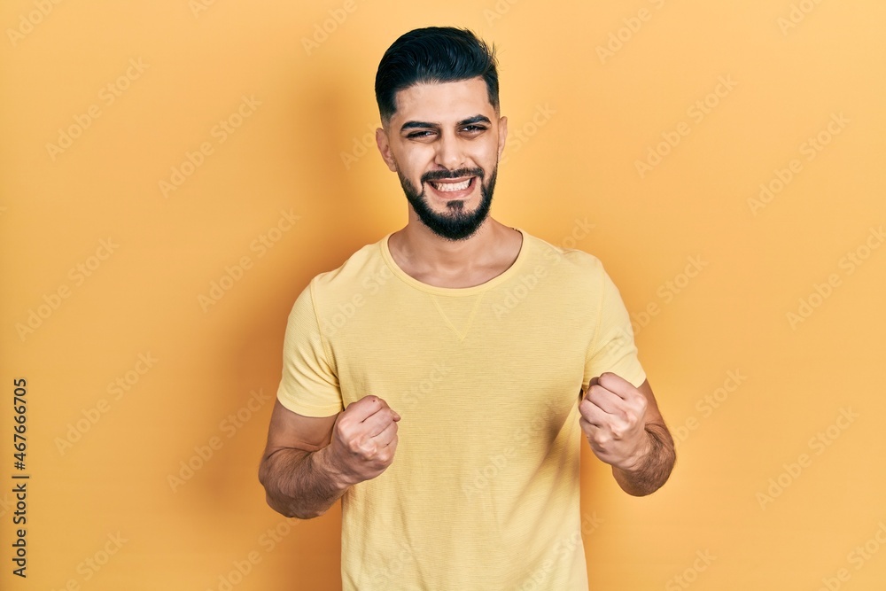 Handsome man with beard wearing casual yellow t shirt excited for success with arms raised and eyes closed celebrating victory smiling. winner concept.