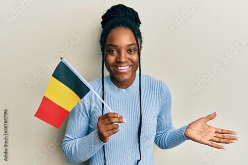 African american woman with braided hair holding belgium flag celebrating achievement with happy smile and winner expression with raised hand