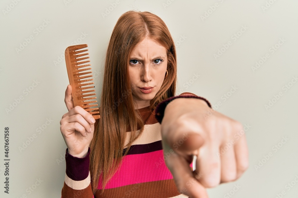 Young irish woman styling hair using comb pointing with finger to the camera and to you, confident gesture looking serious Young irish woman styling hair using comb pointing with finger to the camera and to you, confident gesture looking serious