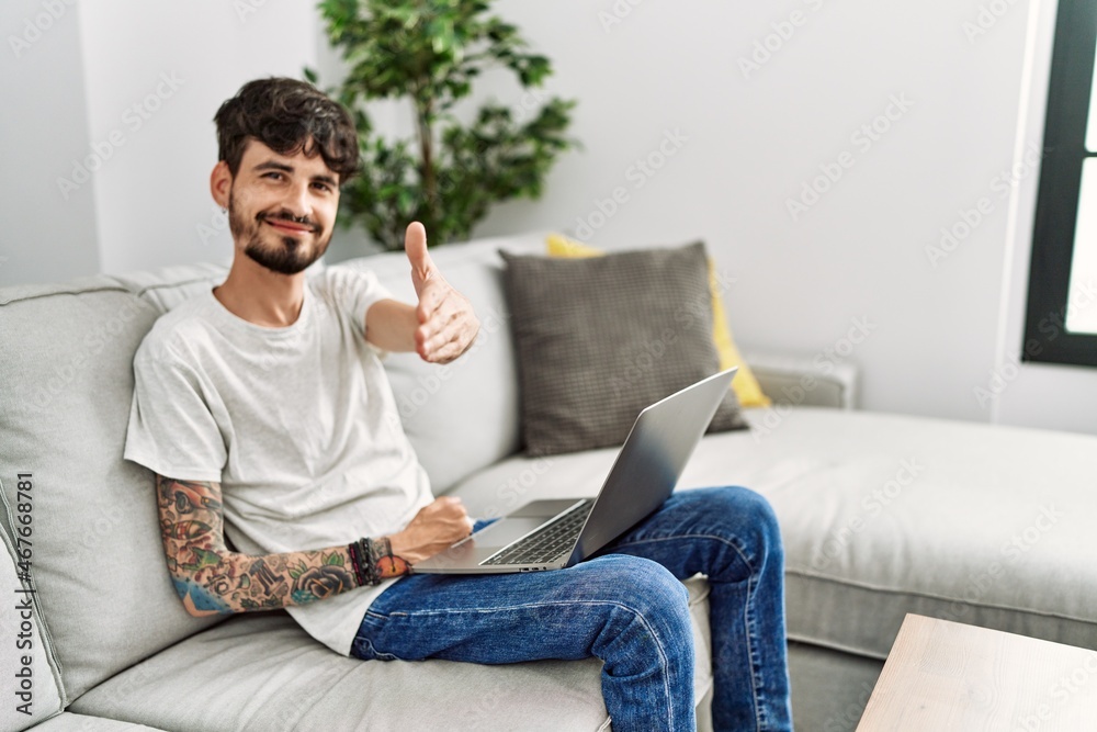 Hispanic man with beard sitting on the sofa smiling friendly offering handshake as greeting and welcoming. successful business.