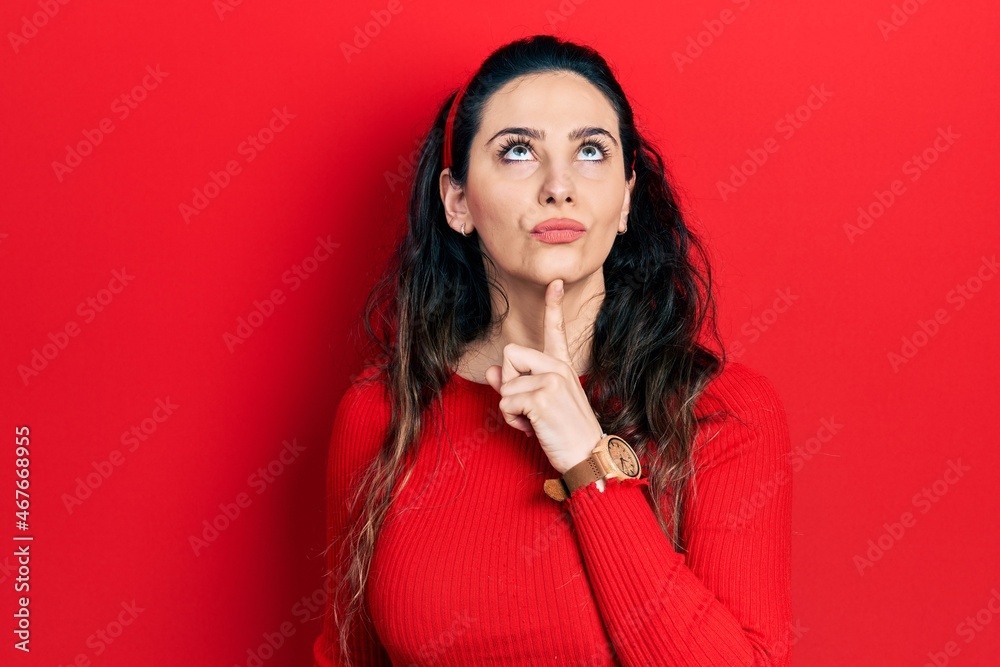 Young hispanic woman wearing casual clothes thinking concentrated about doubt with finger on chin and looking up wondering Young hispanic woman wearing casual clothes thinking concentrated about doubt with finger on chin and looking up wondering