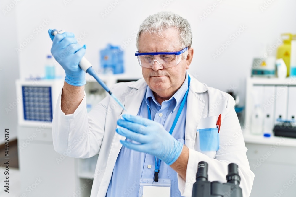 Middle age grey-haired man wearing scientist uniform using pipette at laboratory Middle age grey-haired man wearing scientist uniform using pipette at laboratory