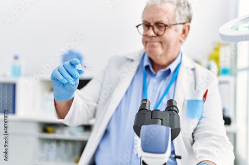 Middle age grey-haired man wearing scientist uniform using microscope at laboratory