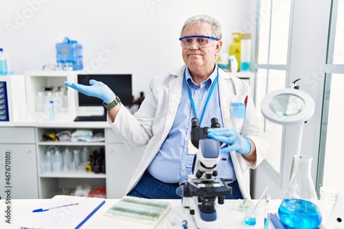 Senior caucasian man working at scientist laboratory smiling cheerful presenting and pointing with palm of hand looking at the camera.