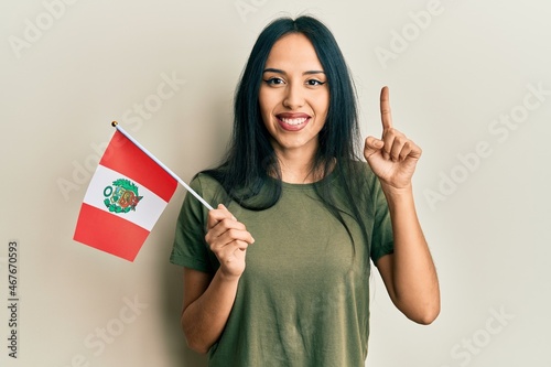 Young hispanic girl holding peru flag smiling with an idea or question pointing finger with happy face, number one