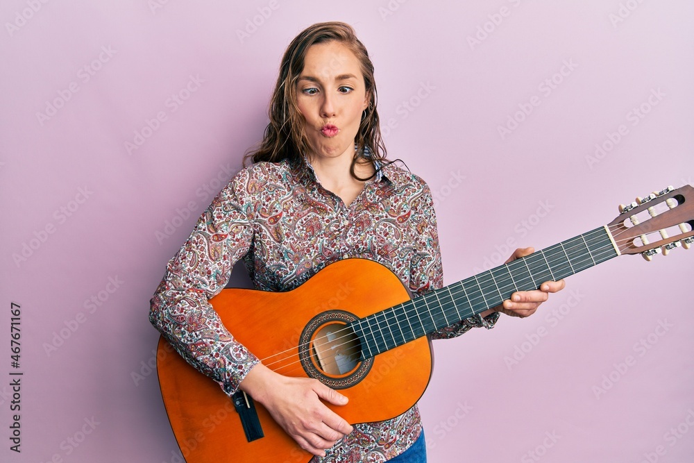 Young blonde woman playing classical guitar making fish face with mouth and squinting eyes, crazy and comical. Young blonde woman playing classical guitar making fish face with mouth and squinting eyes, crazy and comical.