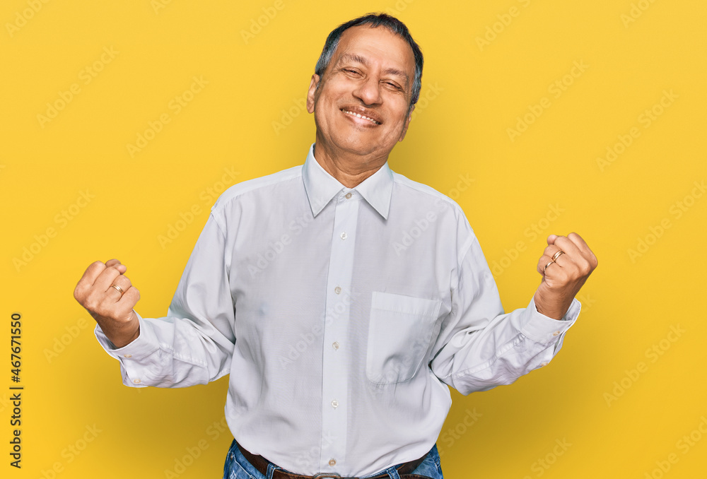 Middle age indian man wearing casual white shirt very happy and excited doing winner gesture with arms raised, smiling and screaming for success. celebration concept. Middle age indian man wearing casual white shirt very happy and excited doing winner gesture with arms raised, smiling and screaming for success. celebration concept.