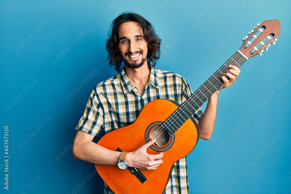 Obraz premium Young hispanic man playing classical guitar smiling with a happy and cool smile on face. showing teeth.