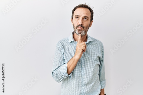 Middle age hispanic man with beard standing over isolated background thinking concentrated about doubt with finger on chin and looking up wondering