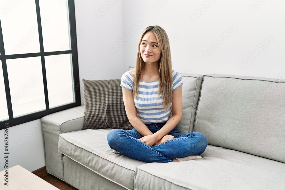 Asian young woman sitting on the sofa at home smiling looking to the side and staring away thinking. Asian young woman sitting on the sofa at home smiling looking to the side and staring away thinking.