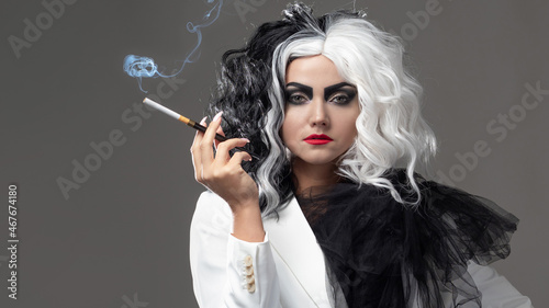 A fatal beauty in a daring fashion image with black and white hair. A rebellious stylish image for Halloween. a young woman in a black and white outfit smokes a cigarette using a mouthpiece photo
