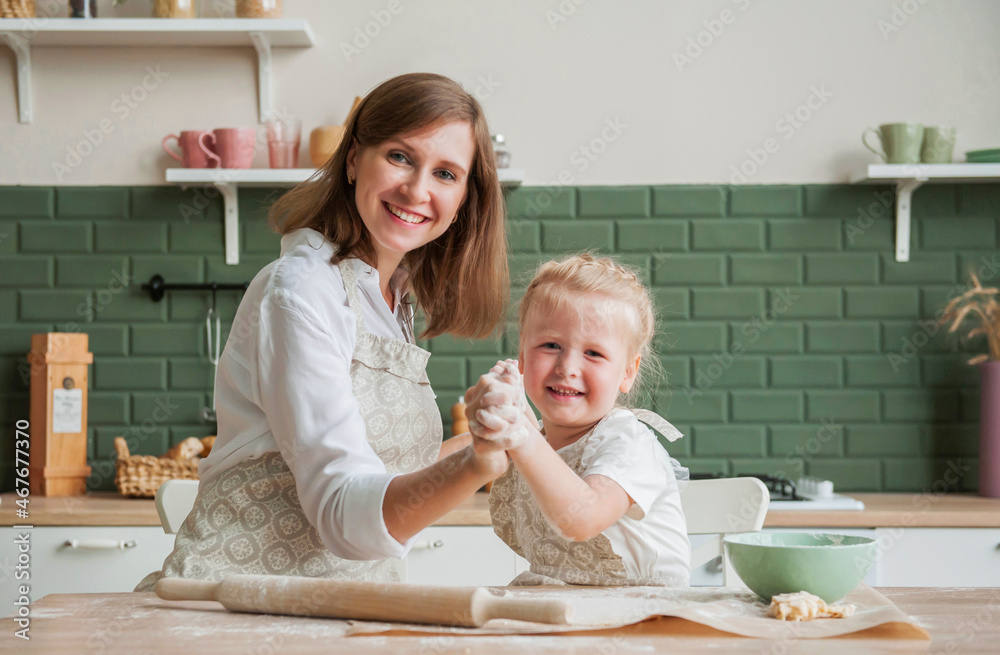 A young mother and her little daughter are cooking together in the kitchen. Mom and child prepare baking dough at home A young mother and her little daughter are cooking together in the kitchen. Mom and child prepare baking dough at home