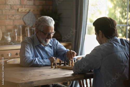 Battle at chessboard. Enthusiastic old father play friendly chess match at home with grownup son. Happy diverse generation male relatives elder younger passionate players meet at chessboard on weekend