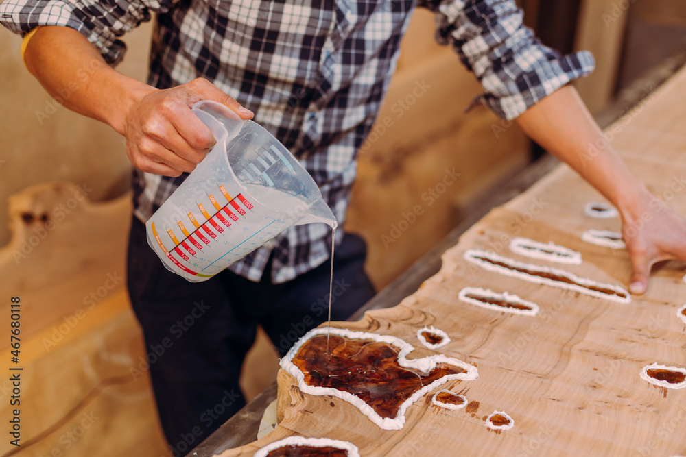 Closeup of carpenter pouring epoxy liquid in a wooden table