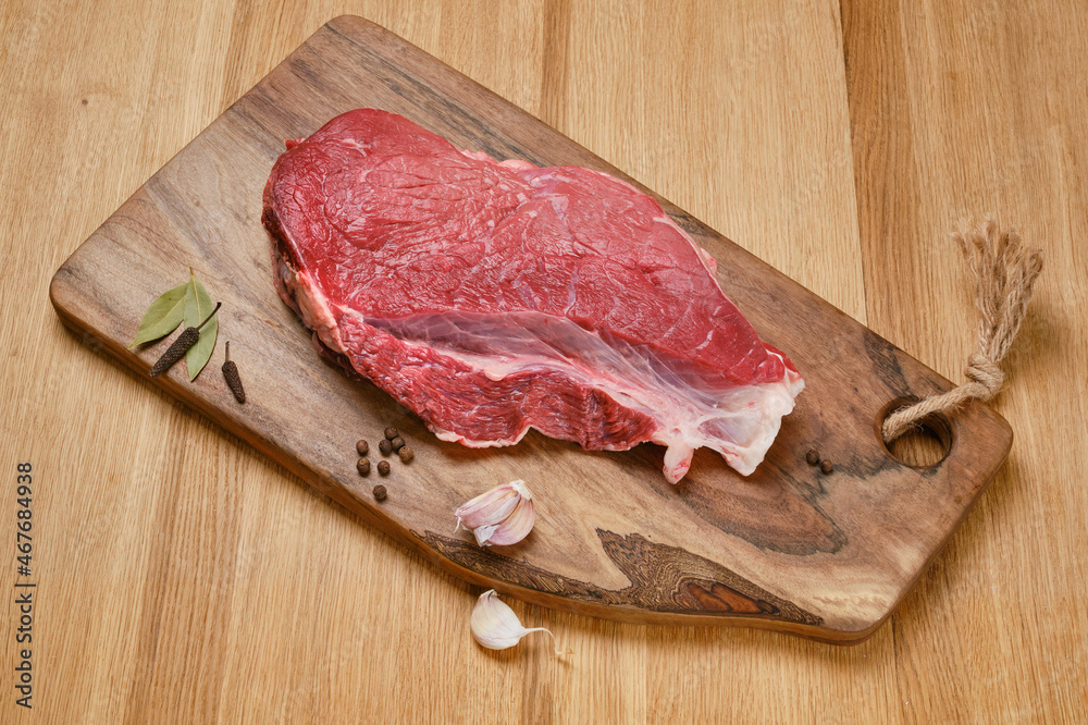Fresh cut of beef on wooden kitchen board with spices. Raw steak on cutting board ready to cook. Selective focus