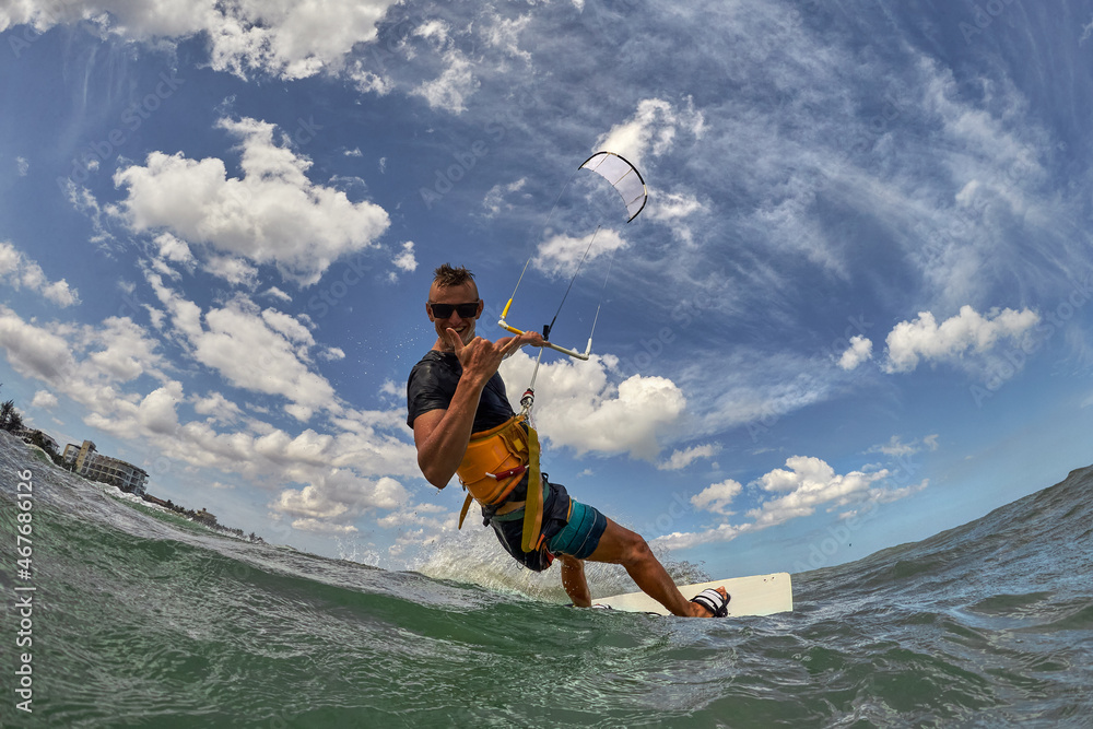 Kite surfer jumps with kiteboard in transition and shows the shaka sign with his fingers