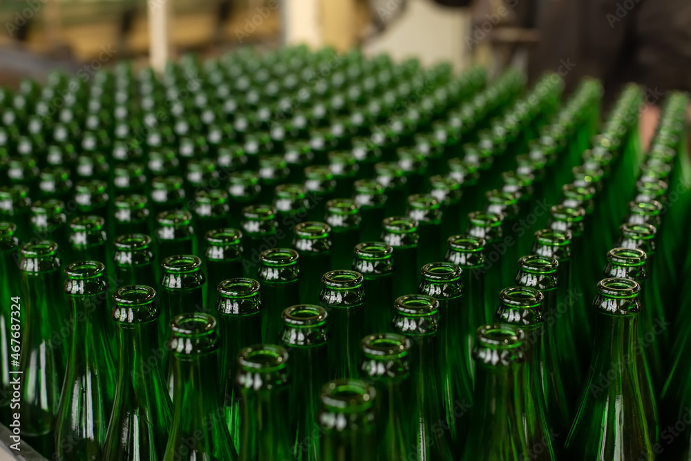 Fototapeta premium Glass factory, industrial production of glass containers. A lot of empty glass bottles as a background of green glass containers with copy space. Bottles for drinks. Technological work at the factory.